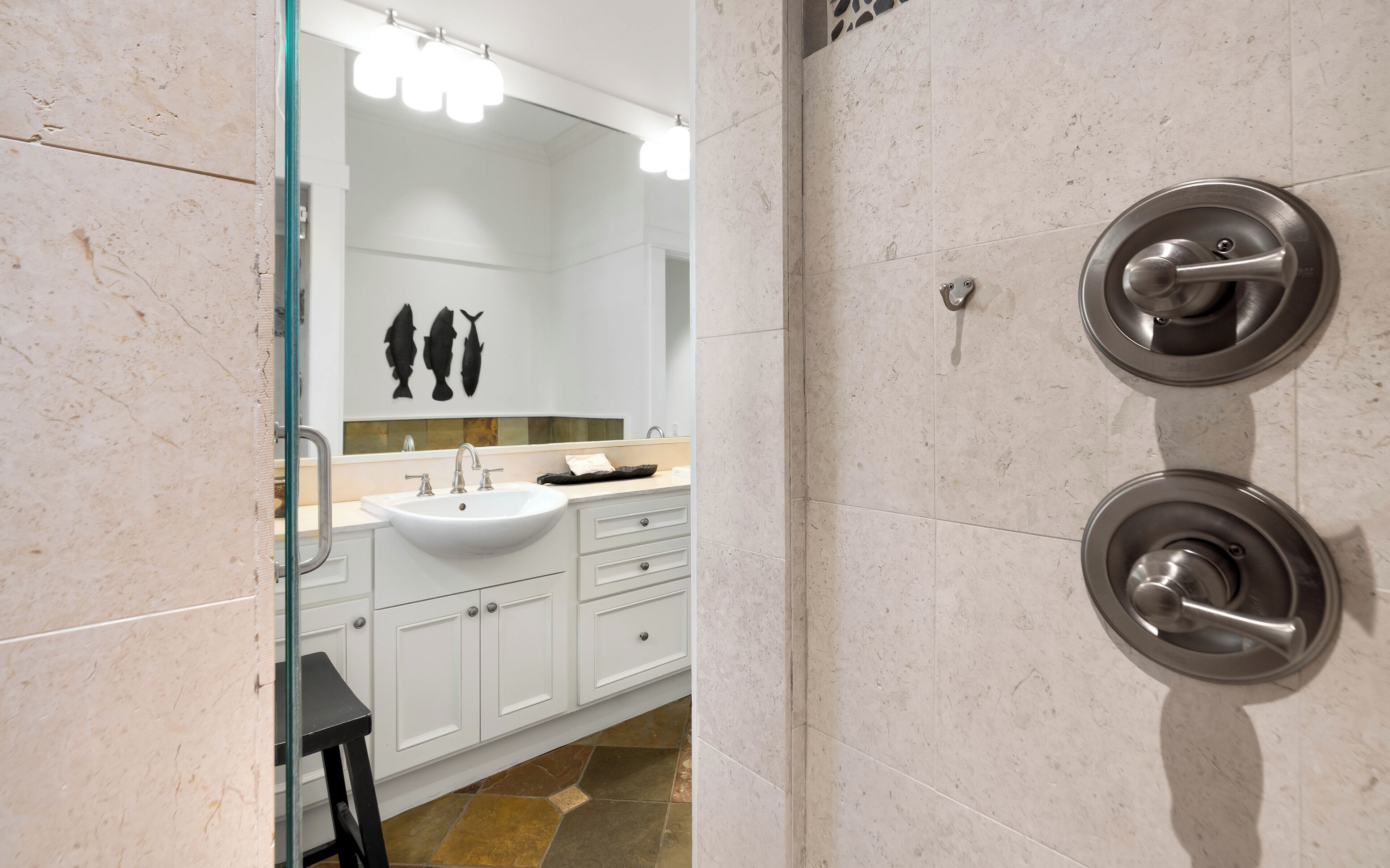 A bathroom with a white sink, a mirror, and a shower with a circular handle.