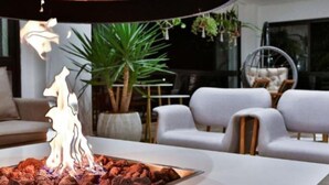 Ein modernes Wohnzimmer mit einer zentralen Feuerstelle, weißen Sofas, einem runden Tisch und einem großen Fenster.