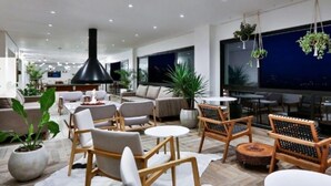 Ein modernes Wohnzimmer mit Sofas, Sesseln und einer großen schwarzen Lampe. Ücht Topfpflanzen und Blick auf den Nachthimmel durch große Fenster.