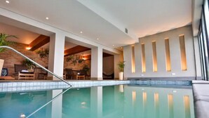 Ein beheiztes Hallenbad mit klarem Wasser, umgeben von Liegebereichen mit Sitzgelegenheiten und Pflanzen.