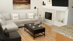 Ein modernes Wohnzimmer mit einem Ecksofa, einem Couchtisch, einem Kamin und einem großen Fernseher, der darüber angebracht ist.