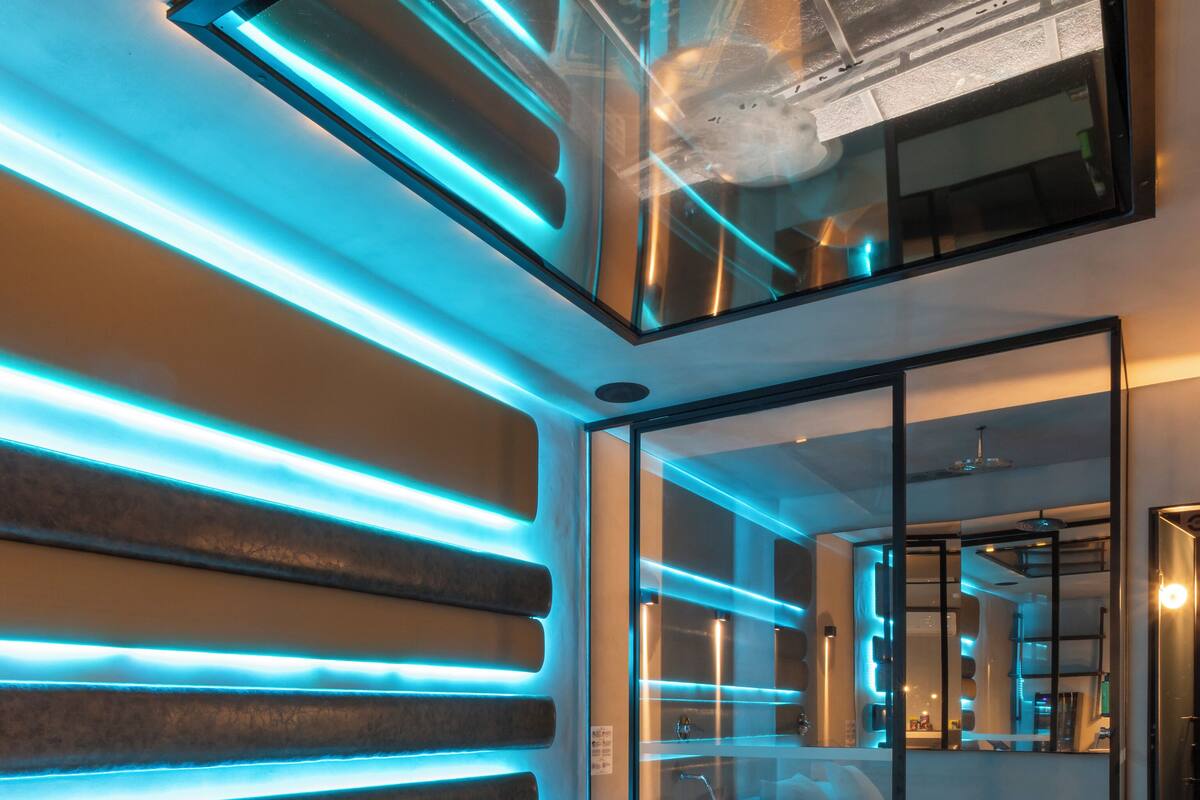 A modern hotel room with a large bed, a glass partition, and ambient lighting.