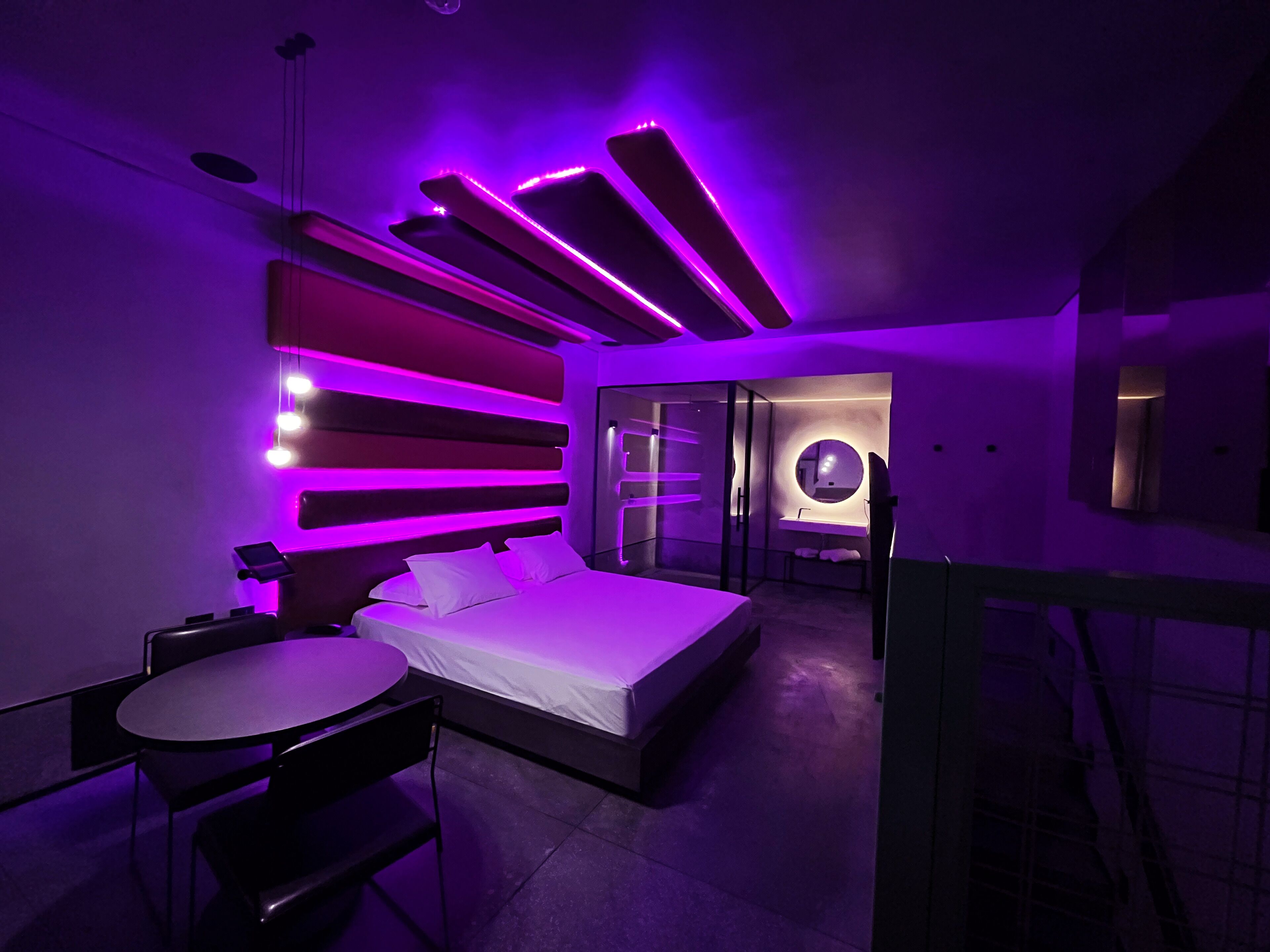 A modern bedroom with a bed, a small table, and a glass-enclosed bathroom.