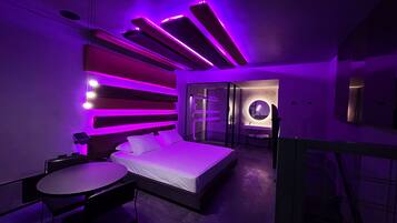 A modern bedroom with a bed, a small table, and a glass-enclosed bathroom.