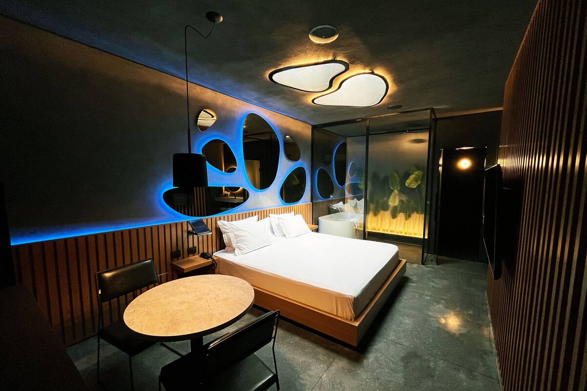 A modern hotel room with a bed, bedside table, chair, and a unique wall design.