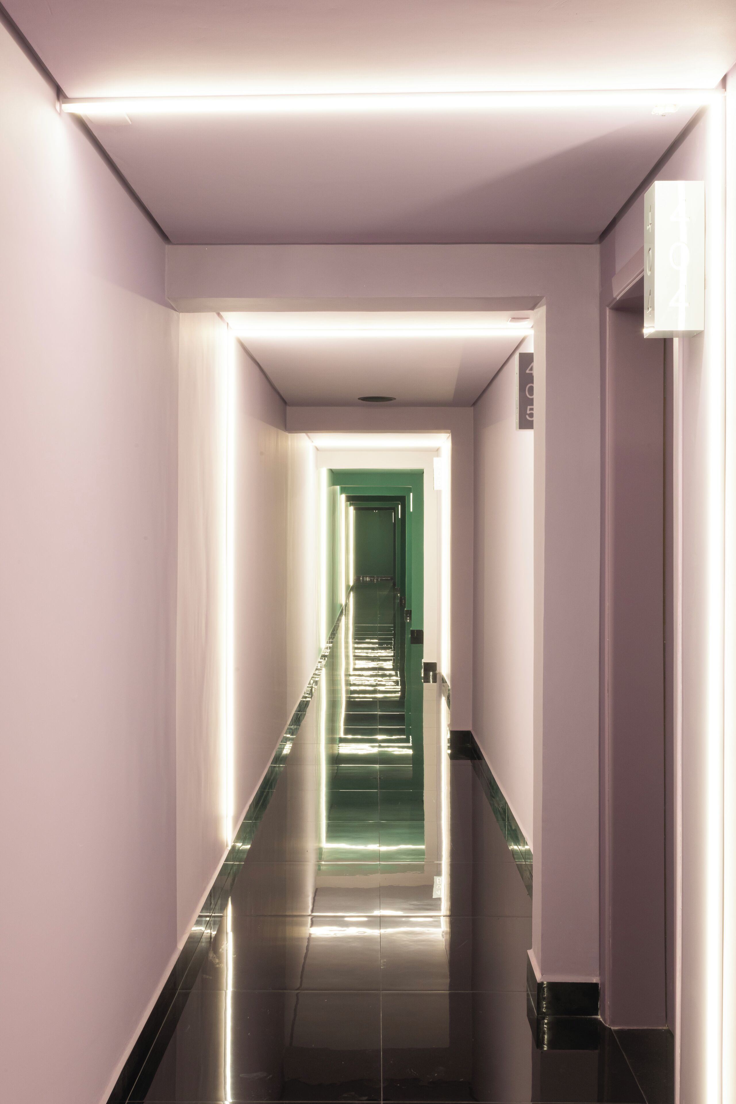 A corridor with a reflective floor and walls, leading to a green door at the end.