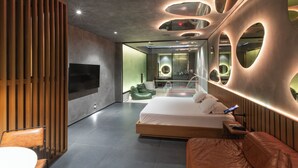 A modern bedroom with a large bed, a TV, and a seating area with a table and chairs.