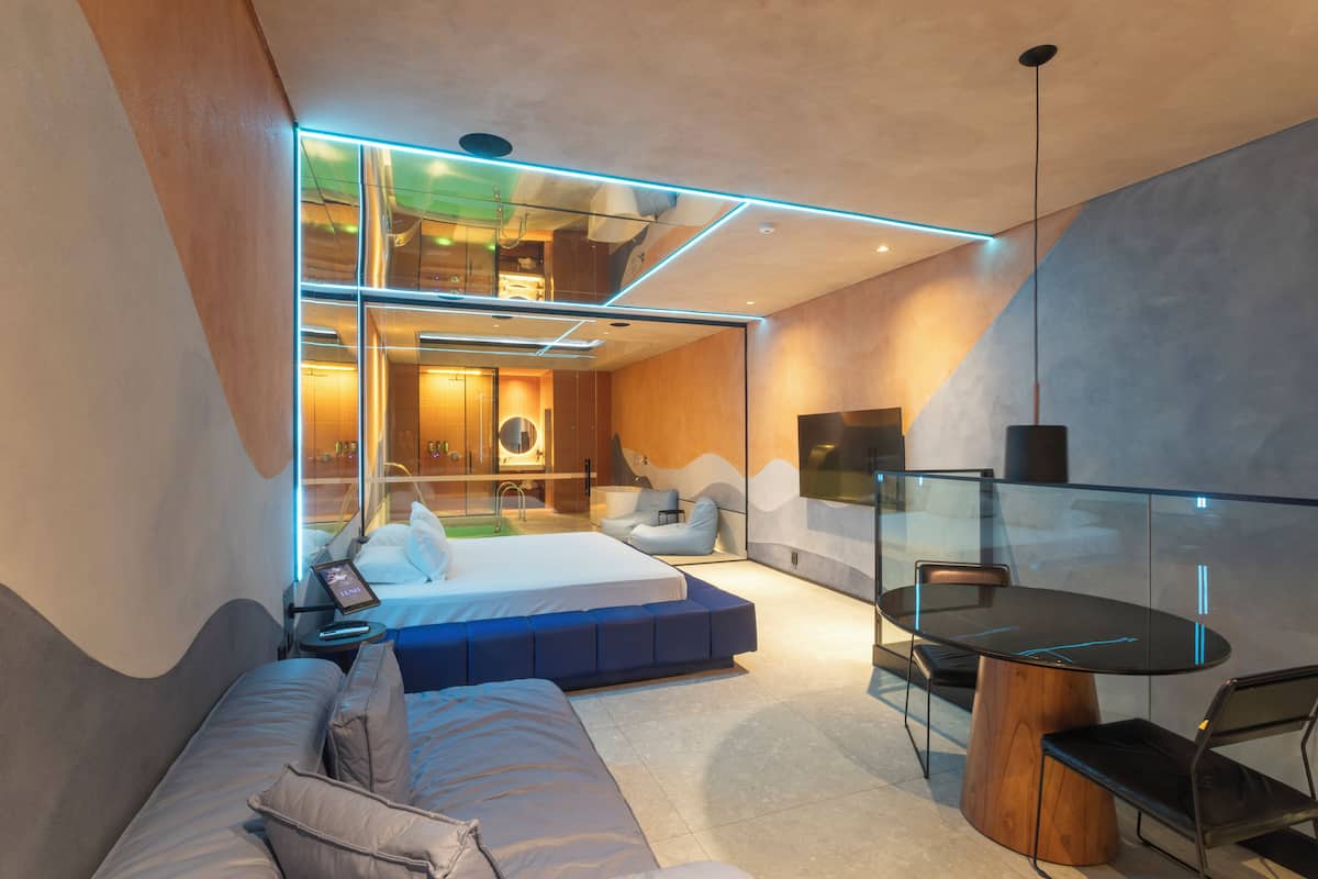A modern bedroom with a bed, seating area, and a dining table.