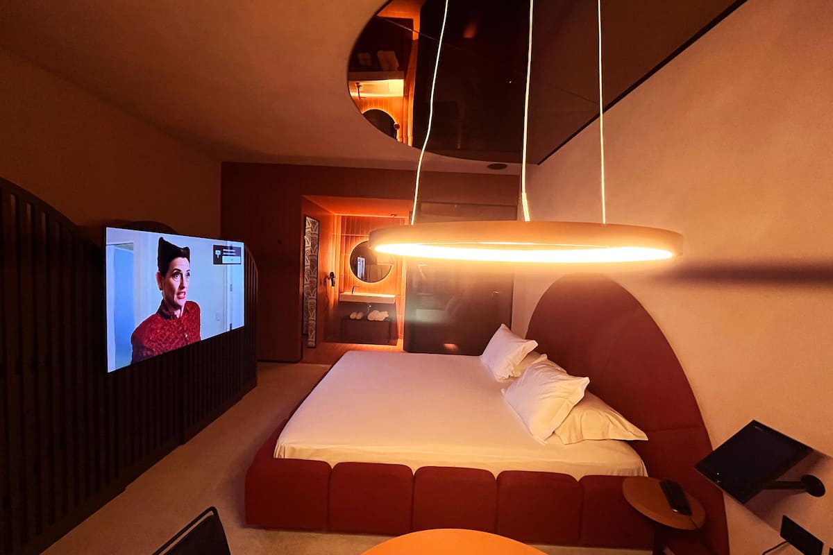 A modern bedroom with a large bed, a television, and a bedside table with a lamp.