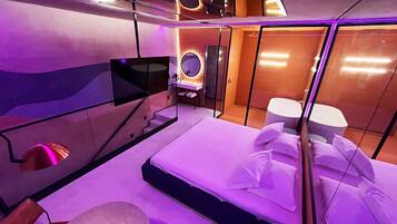 Un dormitorio moderno con cama, televisión, espejo y zona de ducha.
