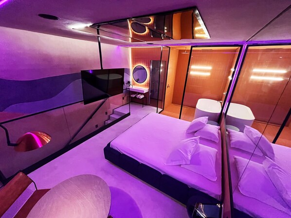 A modern bedroom with a bed, a TV, a mirror, and a shower area. - Lush Motel Lapa (São Paulo)