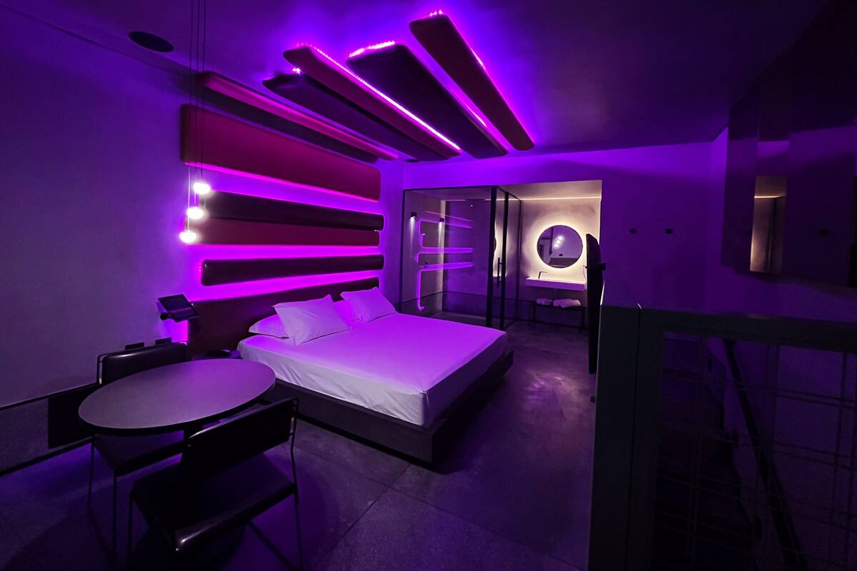A modern bedroom with a bed, bedside table, and a bathroom with a round mirror.