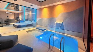 Una habitación de hotel moderna con un ventanal grande, un escritorio integrado, una cama y un pequeño espacio con piscina.