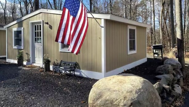 Ein kleines, eingeschossiges Gebäude mit einer beige farbenen Fassade und einer Fahnenstange mit der US-Flagge.