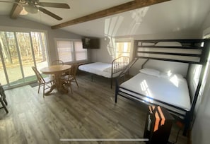 Een kamer met een stapelbed, een bureau met een stoel, een televisie en grote ramen.