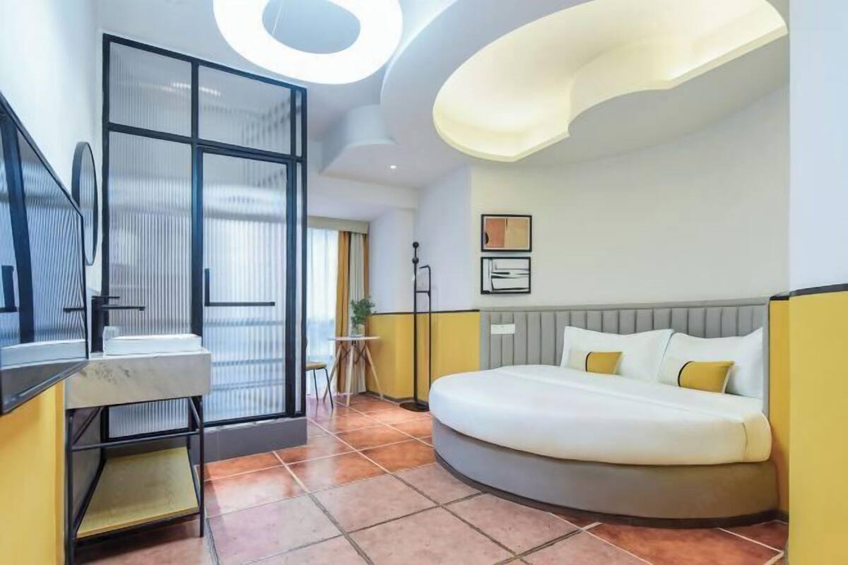 Un dormitori modern amb un llit corbat, una separació de vidre i una làmpada de sostre rodona.
