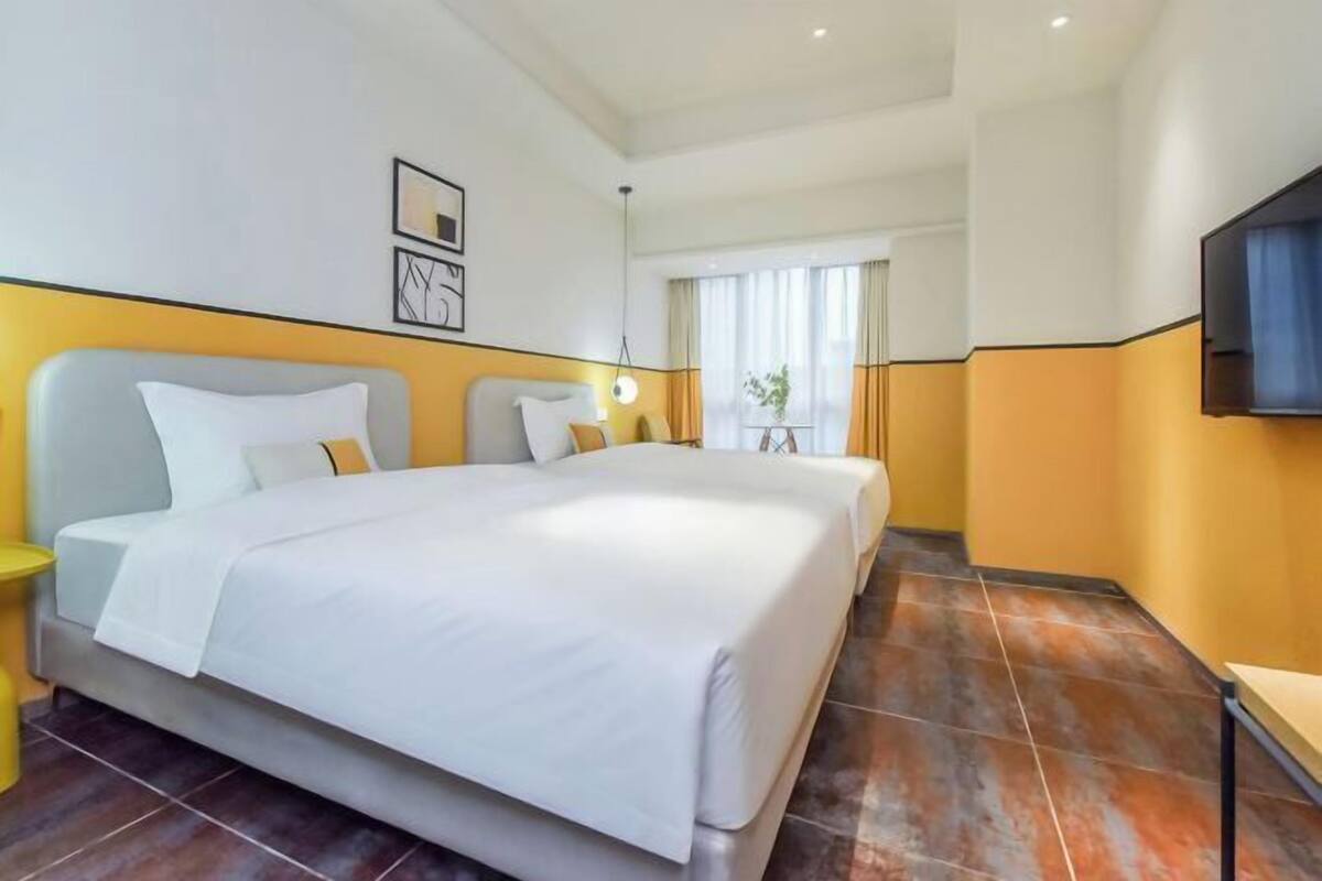 Habitació d'hotel amb un llit gran, un televisor fixat a la paret i una finestra amb cortines.