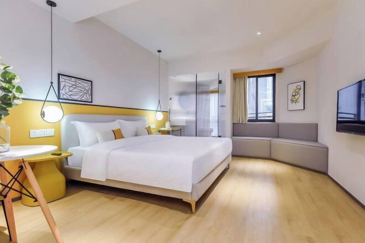 Habitació d'hotel moderna amb un llit gran, una zona de seients corba, un televisor de pantalla plana i una taula petita amb una planta.