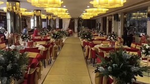 Un pasillo de hotel con mesas y sillas, un camino central e iluminación decorativa.