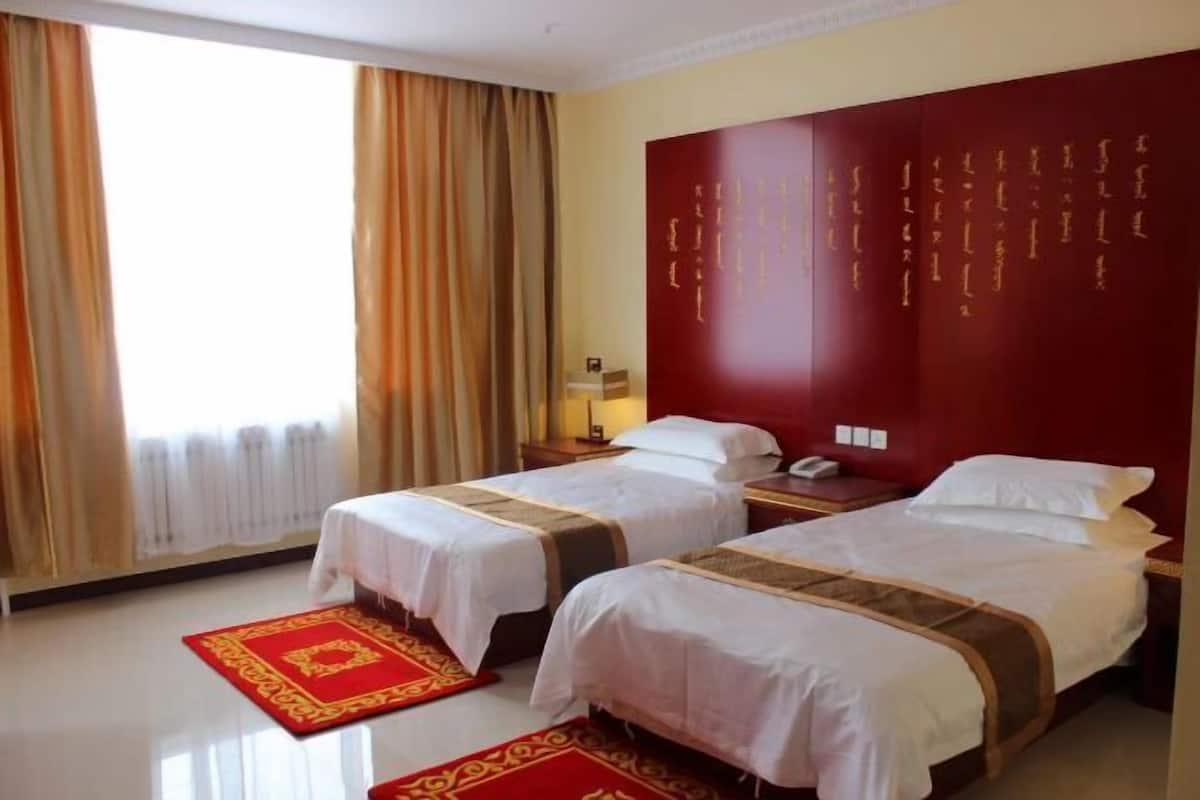 A hotel room with two beds, a red accent wall, and a window with curtains.