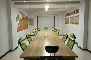 Une salle de conférence avec une longue table et des chaises vertes, des murs blancs et un écran de projection.
