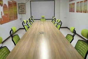 Une salle de conférence avec une longue table et des chaises vertes, un écran de projection et des affiches aux murs.
