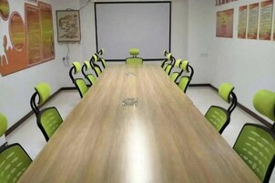 Un salón de conferencias con una larga mesa y sillas verdes, una pantalla de proyector y carteles en las paredes.