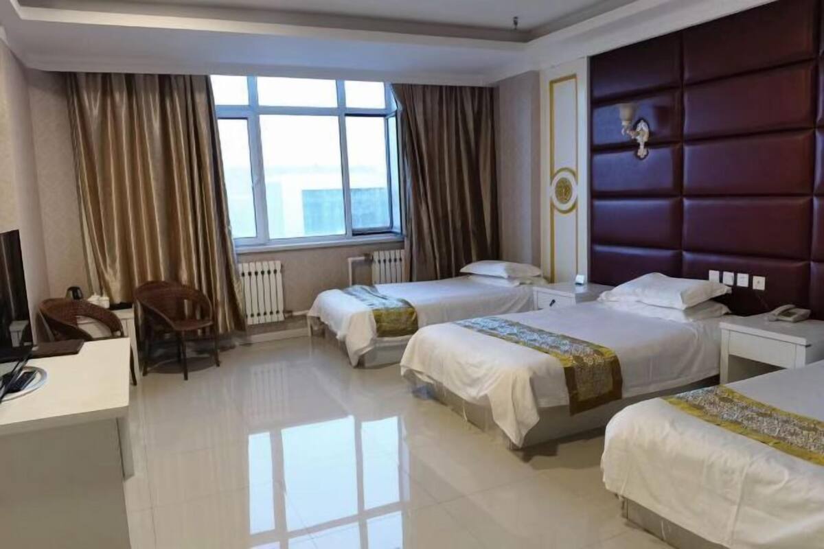 A hotel room with two beds, a desk, a chair, and a large window.