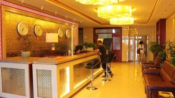 A hotel reception area with a reception desk, two bar stools, a clock, and a chandelier.