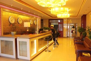 A hotel reception area with a reception desk, two bar stools, a clock, and a chandelier.