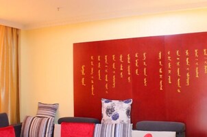 A hotel room with a red accent wall featuring gold calligraphy, a striped pillow, and a floral pillow on a sofa.