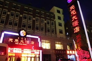 Un edificio con letreros iluminados, un cartel vertical destacado con caracteres chinos, y un autobús estacionado al frente.