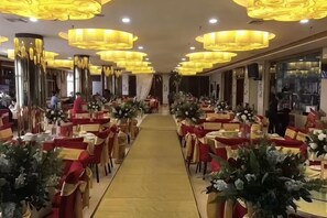 A hotel dining area with tables arranged in rows, a central walkway, and decorative lighting.