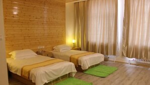 Una habitación con dos camas, paredes de madera, un ventanal con cortinas y una alfombra verde.