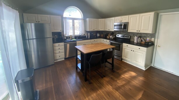 A kitchen with white cabinets, a stainless steel refrigerator, a wooden dining table, and a ceiling fan.