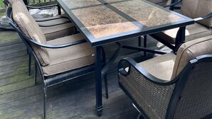 An outdoor patio with a table and chairs, a red umbrella, and a barbecue grill.