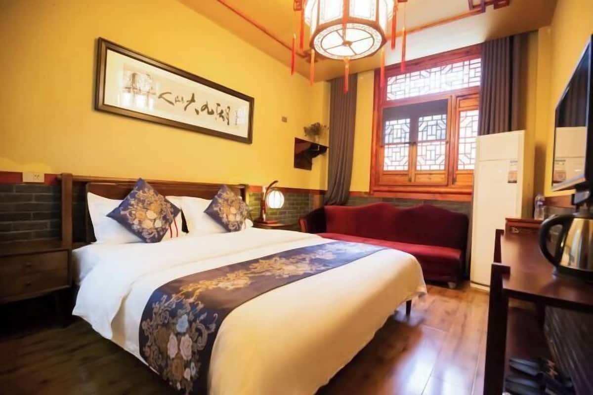 A hotel room with a bed, a red sofa, a wooden cabinet, and a wall-mounted picture.