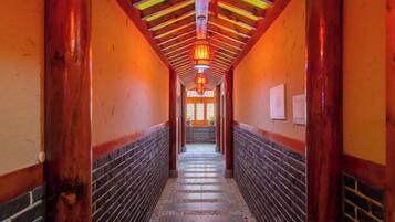 A corridor with wooden beams and a tiled floor, leading to a door with a red lantern.