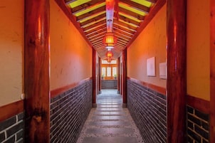 A corridor with wooden beams and a tiled floor, leading to a door with a red lantern.