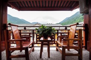 A wooden balcony with a table and chairs, a potted plant, and a view of mountains.