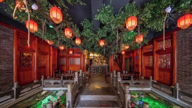 Un corredor al estilo chino tradicional con puertas de madera, linternas y una fuente central.