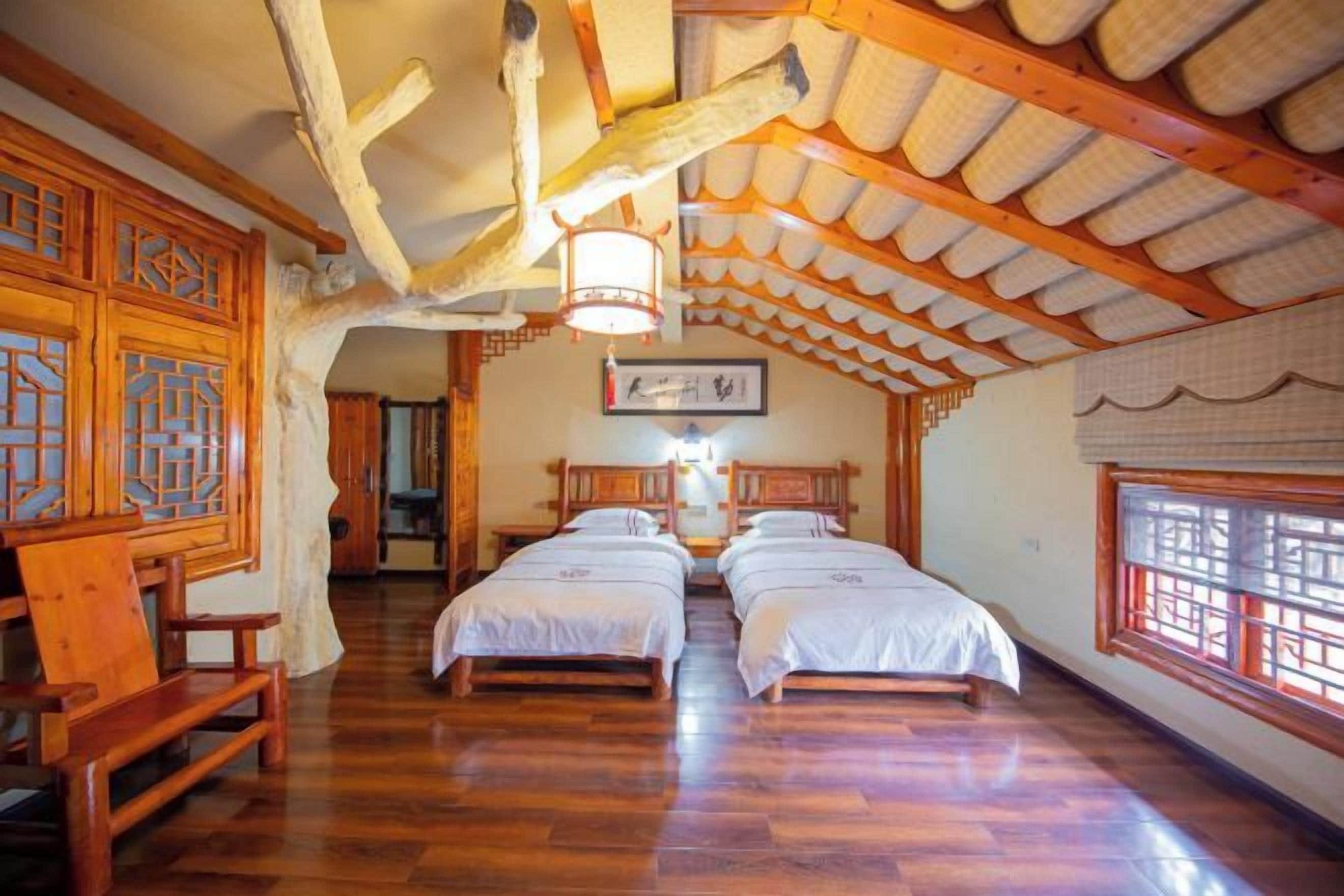 A traditional room with wooden floors, two beds, a wooden bench, and a ceiling with exposed beams and a hanging light fixture.