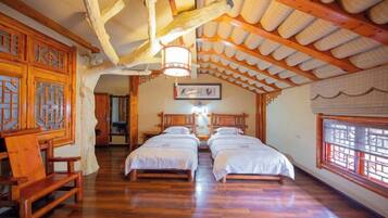 A traditional room with wooden floors, two beds, a wooden bench, and a ceiling with exposed beams and a hanging light fixture.