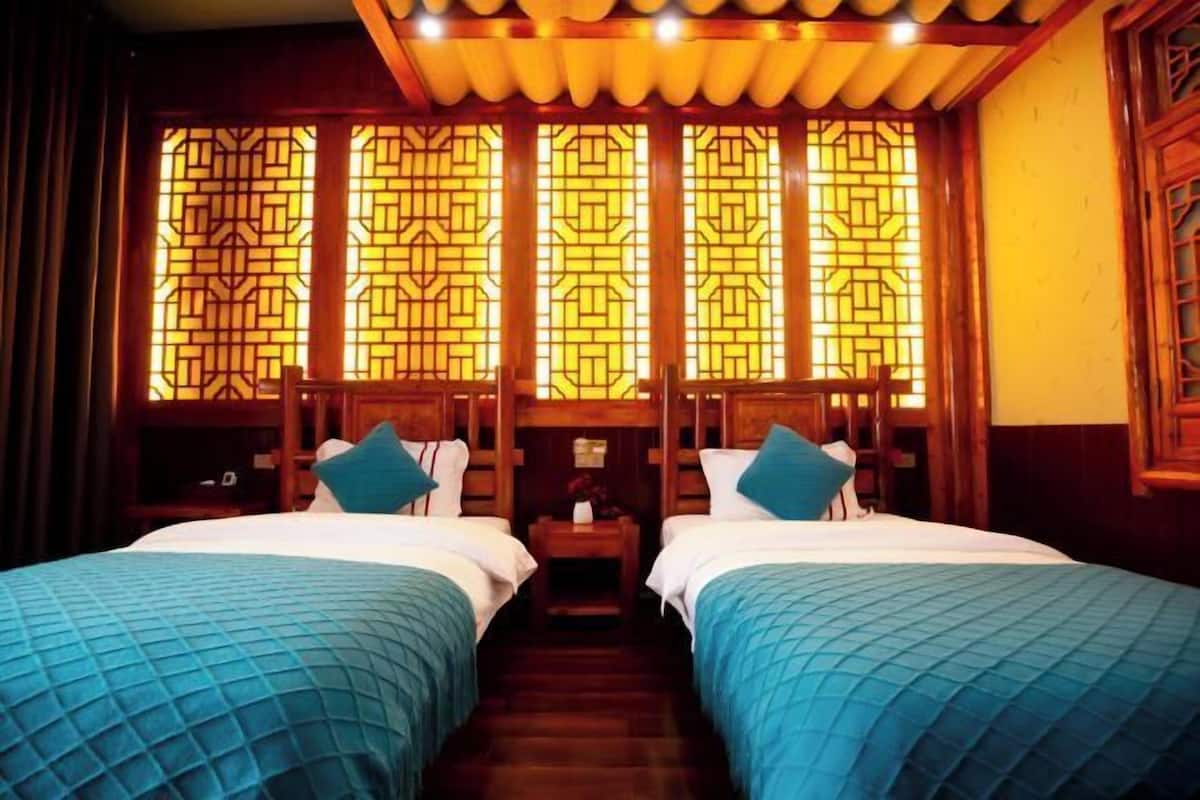 A hotel room with two beds, wooden headboards, and a traditional Chinese window design.