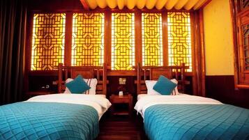 A hotel room with two beds, wooden headboards, and a traditional Chinese window design.