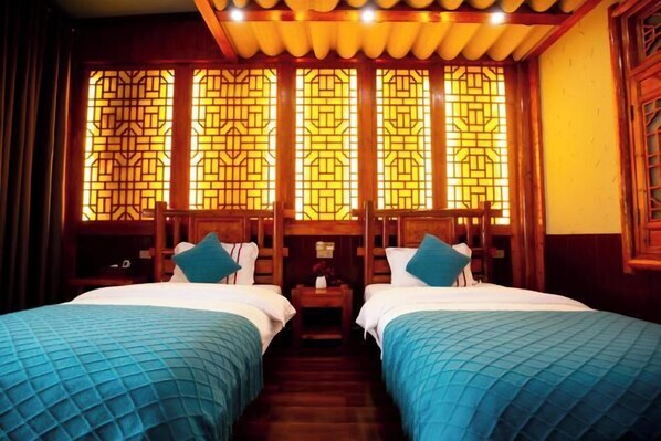 Habitación de hotel con dos camas, cabeceros de madera y diseño tradicional de ventana china.