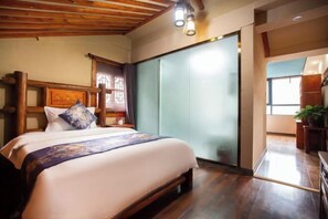 Un dormitorio con cabecera de madera, cama con edredón floral y un armario de puertas correderas, con vistas a la cocina a través de un vano abierto.