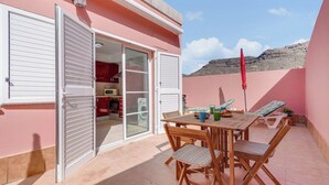 A pink building with a patio area featuring a table and chairs, a red umbrella, and a view of a mountain. - Home2Book Comfy Apt Puerto Rico, Pool&Terrace (Mogán)