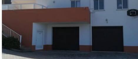 Un bâtiment à deux étages, doté d’un toit plat, de deux portes de garage et d’un petit balcon à l’étage supérieur.