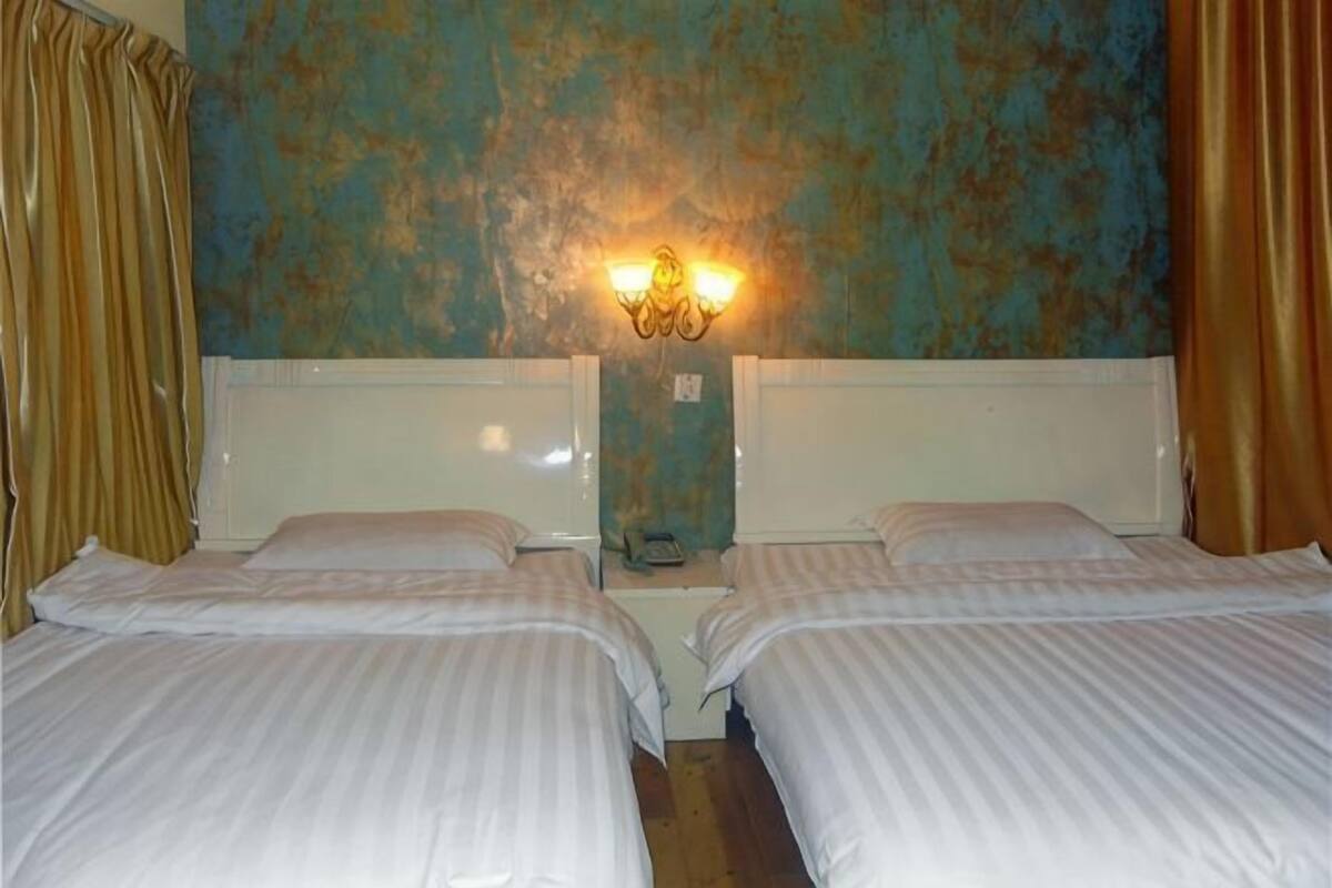 Une chambre avec deux lits, un luminaire fixé au mur et des rideaux.